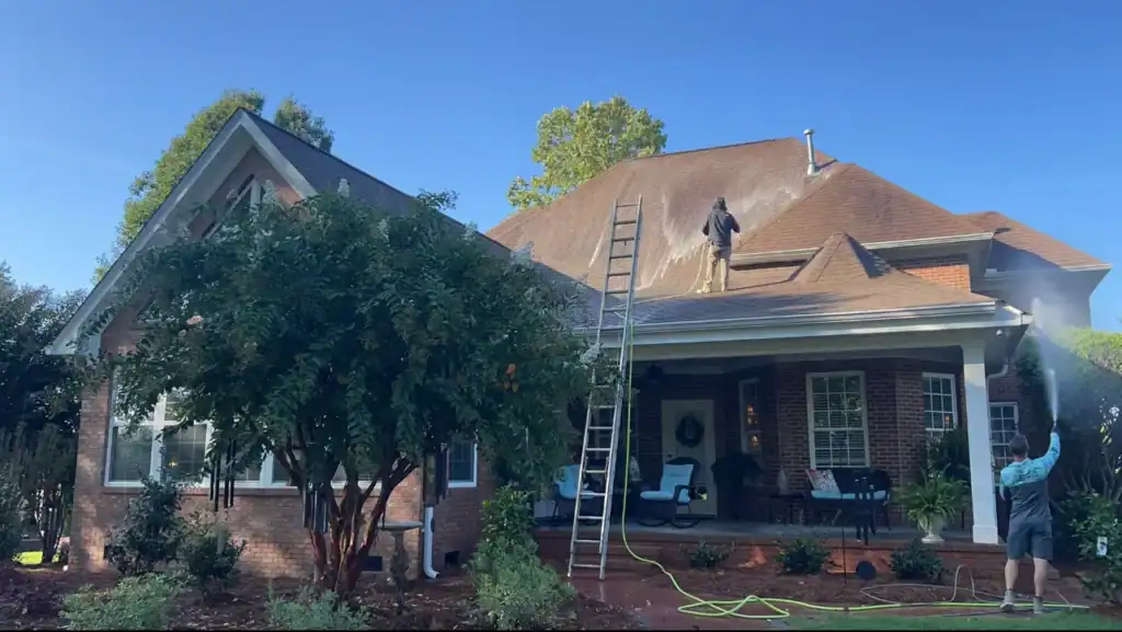 Technicians soft washing a roof on a brick home in Greenville SC